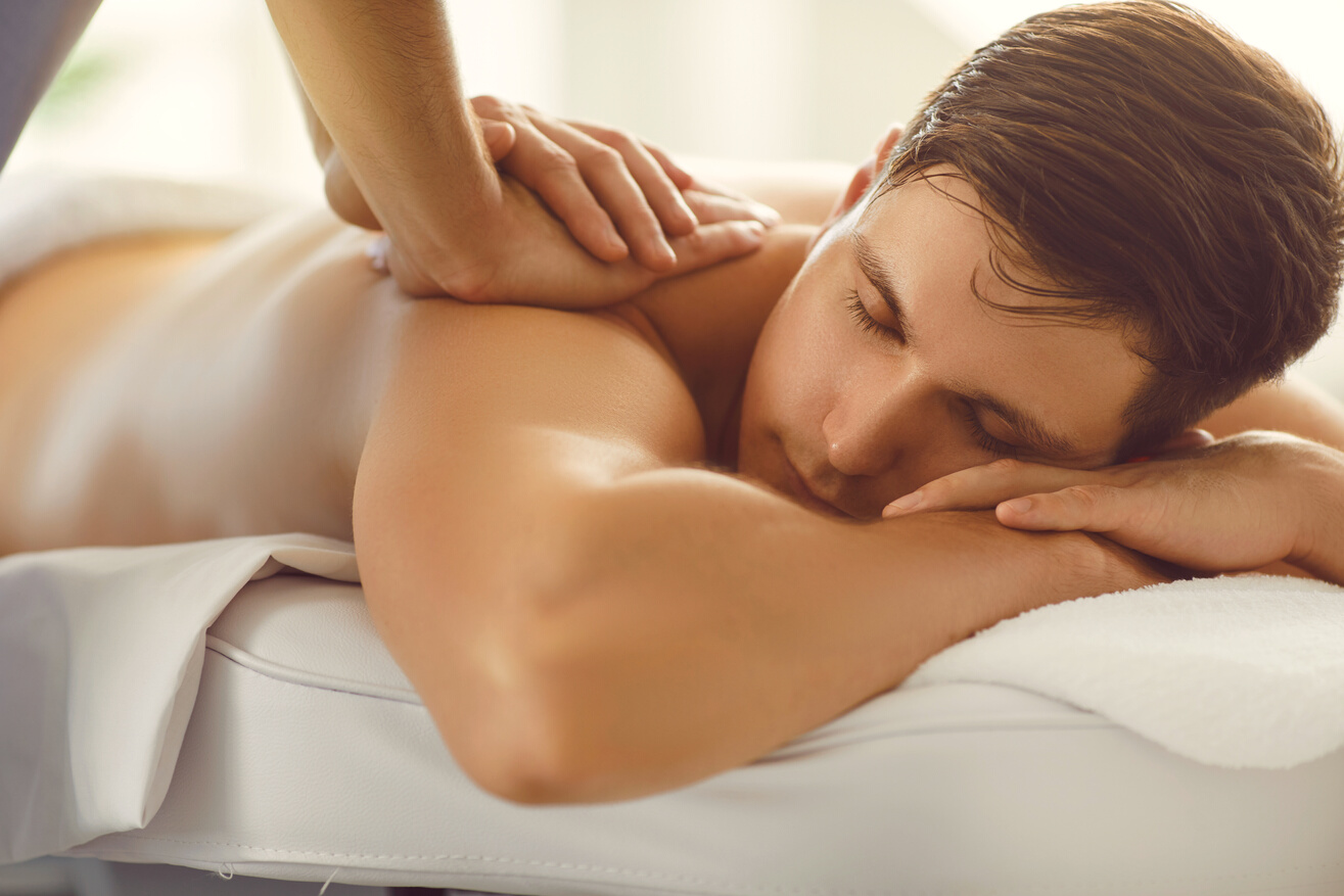 Young Man Lying on Massage Table with Eyes Closed Enjoying Professional Relaxing Back Massage